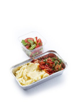 Beyaz arka planda tek kullanımlık plastik ve folyo sofra takımı yiyecek patates püresi ve taze sebzeli tavuk filetosu.