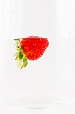 Beyaz bir fotografın arka planında olgun bir çilek, berrak sularda böğürtlen ve meyve yıkıyor sağlıklı vitaminler mevsimlik yaz meyveleri C vitamini, yeşil çilek kuyruğu, taç gibi.