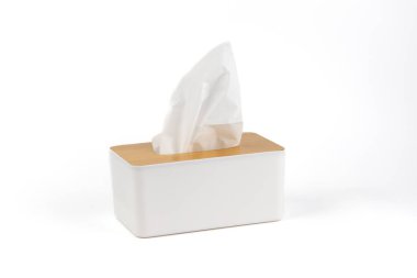 Beyaz arka planda beyaz bir plastik peçete tutacağı duruyor. Tahta kapaklı, minimalist bir tasarımı var. Beyaz peçete hijyen setini dışarı çıkarıyor.