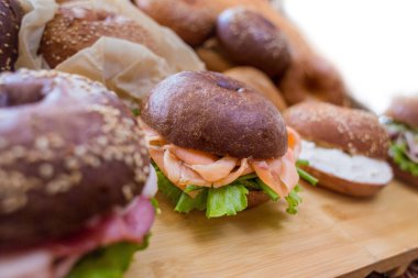 Tahta suşi tezgahında yakın beyaz bir plan. Kırmızı balık ve tilki salatasıyla dolu neredeyse üç simit var. Sağlıklı, yüksek kalorili, sağlıklı kahvaltı.