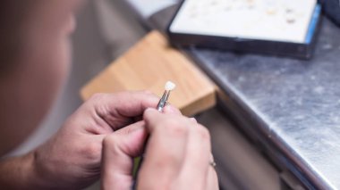 Diş implantı, protez ve kaplama üretimi için profesyonel bir laboratuarda yakın plan, bir usta diş implantı, protez ve kaplama üretiminde diş ürünlerinin özgün ve gölgelerini modellemek için bir fırça kullanır.
