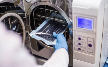 Profesyonel bir laboratuvarda diş implantları, protezler ve kaplamalar yapan bir kız diş aletlerini çalışan bir fırına yerleştirir, steril işler, bireysel ambalajlar