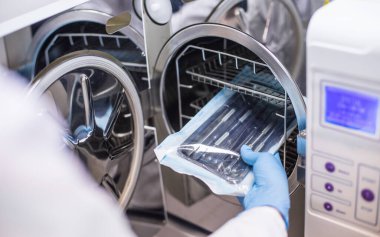 Profesyonel bir laboratuvarda diş implantları, protezler ve kaplamalar yapan bir kız diş aletlerini çalışan bir fırına yerleştirir, steril işler, bireysel ambalajlar