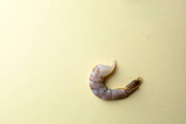 Açık sarı arkaplanda yakın plan nesne fotoğrafçılığı, kafaları olmayan soyulmamış kral karidesleri, yanında taze deniz ürünleri, deniz ürünleri makarnası, koyu kuyruklar.