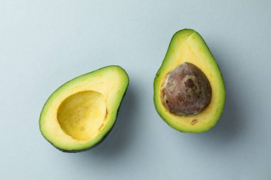 Açık mavi arka planda bulunan bir nesnenin yakın plan fotoğrafı, yeşil, yuvarlak, olgun taze bir avokadonun iki yarısı, çukur olsun ya da olmasın, protein ve amino asit açısından zengin sağlıklı yiyecekler içerir.
