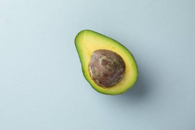 Açık mavi arka plandaki bir nesnenin yakın plan fotoğrafı yeşil, olgun, taze bir avokado, proteinler ve egzotik sebze soslu amino asit salatası zengini.