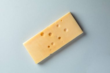 Açık mavi arkaplanda bulunan bir nesnenin yakın plan fotoğrafı süt ürünü atıştırmalıkları ve şarap laktoz ürünlerine karşı hayvansal yağlarla dilimlenmiş bir peynir parçası uzanıyor.