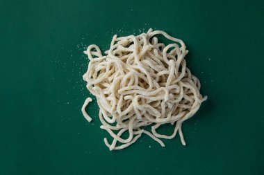 Koyu yeşil arka planda, rendelenmiş parmesan peynirli İtalyan mutfak robotu kırıntıları serpiştirilmiş, el yapımı spagetti serpiştirilmiş bir nesnenin yakın plan fotoğrafı.