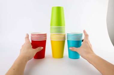 kahve ve çay için beyaz arka plan kağıt bardak yığını kırmızı sarı ve mavi renklere boyanmış yemek takımı özellikleri geziler için eğlence ve piknik için ekolojik fincanlar kadın elleri onları alır