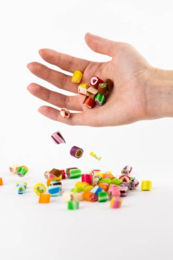 Beyaz bir arka planda, küçük bir avuç içinde farklı aromalı ve resimli çok renkli karameller, çocukların en sevdiği şekerler kan şekerinin aşırı ağırlığı riskini taşır.