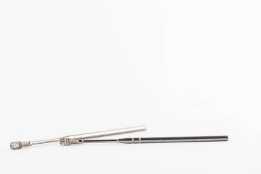 Beyaz arka planda, kulak hastalıklarının kulak açıcı önleminden toprak çıkarmak için bir spiral içeren demir modern kulak çubukları uzanıyor.