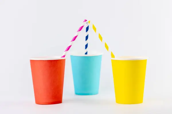 Beyaz arka planda üç tane kağıt bardak var. Yan yana. Sarı, kırmızı ve mavi.