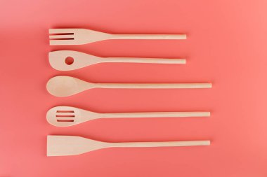 Yumuşak pembe arka planda yakın plan çekimde farklı şekillerde mutfak aydınlığı ahşap çatal bıçaklar farklı şekillerde spatula doğal ahşap kaplama farklı kullanım şekilleri için spatula