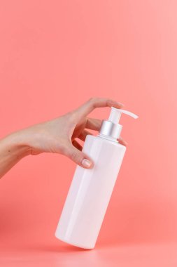 Yumuşak pembe arka plan üzerine yakın plan beyaz parlak şişe kozmetik güzellik endüstrisi için minimalist kap Sıvı hava deposu kadın eli bir parmak ile şeker kutusuna bastırır