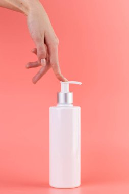 Yumuşak pembe arka plan üzerine yakın plan beyaz parlak şişe kozmetik güzellik endüstrisi için minimalist kap Sıvı hava deposu kadın eli bir parmak ile şeker kutusuna bastırır