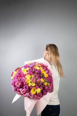 on a light gray background a young blonde girl with a large bouquet of pink peony roses womens holiday March 8 first date the girl stands with her back turned away  clipart