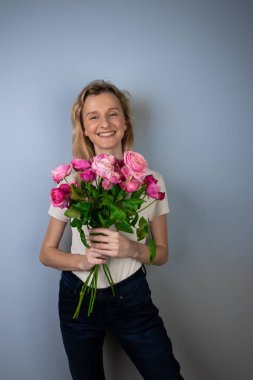 Açık gri bir arka planda büyük bir buket pembe güllü bayanla genç bir sarışın kız tatilinde 8 Mart 'ta gülümseyen kızda ilk randevu duyguları.