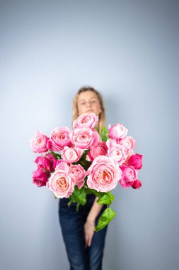 on a light gray background a young blonde girl with a large bouquet of pink peony roses womens holiday the eighth of March first date emotions on the face smiling girl in the background out of focus clipart