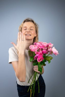 on a light gray background a young blonde girl with a large bouquet of pink peony roses womens holiday March 8 marriage proposal emotions on the face smiling girl hand with a ring clipart