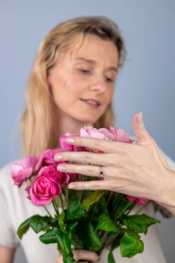 Açık gri bir arkaplanda büyük bir buket pembe güllü bayanla genç bir sarışın kız 8 Mart 'ta evlenme teklif ederken yüzlerinde yüzükle gülümseyen kız eli vardı.