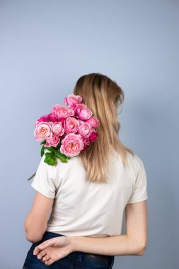 Açık gri bir arka planda büyük bir buket pembe şakayık güllü bayanla genç bir kız tatilde 8 Mart 'ta kız arkasını dönerek duruyor. 