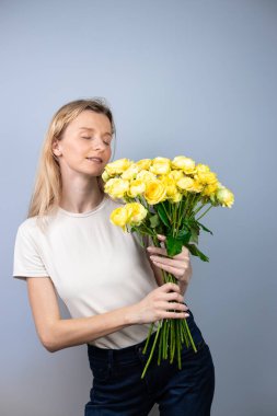 Açık gri bir arka planda, büyük bir buket sarı şakayık güllü bayanlarla genç bir kız tatilinde 8 Mart 'ta ilk buluşmada, gözleri kapalı gülümseyen kız yüzünde duygular belirdi.