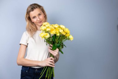 Açık gri bir arka planda büyük bir buket sarı şakayık güllü bayanlarla genç bir kız tatilinde 8 Mart 'ta gülümseyen kızda ilk randevu duyguları.