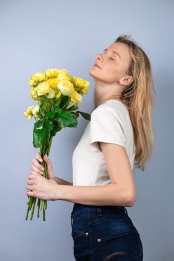 Açık gri bir arka planda büyük bir buket sarı şakayık güllü bayanlarla genç bir kız tatilinde 8 Mart 'ta kız arkasını dönerek ayakta duruyor.