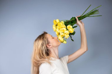 Açık gri bir arka planda büyük bir buket sarı şakayık güllü bayanlarla genç bir kız tatilinde 8 Mart 'ta kız arkasını dönüp çiçekleri kokluyor.