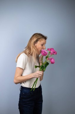 Açık gri arka planda açık renk tişörtlü, pembe şakayık güllü genç bir kız 8 Mart 'ta şok olmuş bir evlilik teklifi sunuyor.