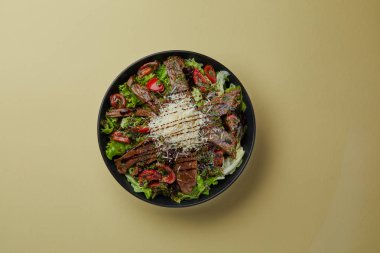 Sarı arka plan siyah salata tabağında, balzamik vişneli, rendelenmiş çedar peynirli, güzel dekore edilmiş ılık dana salatası.