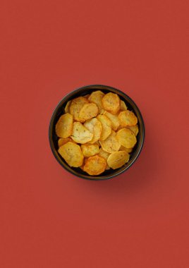 Kırmızı arka planda, siyah tabakta, kızarmış patatesler yuvarlak dilimlerde, rustik tarzda, biberiye serpiştirilmiş, aromatik yan yemek, Avrupa mutfağı.