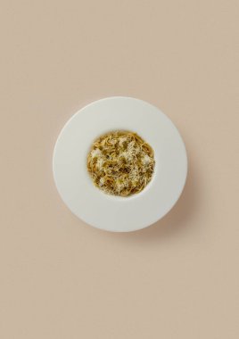 Bej bir arka planda, İtalyan peynirli ve kıymalı makarnalı yuvarlak beyaz bir tabak. Klasik mutfak, buğday, karbonhidrat ve protein açısından zengin yiyecekler..