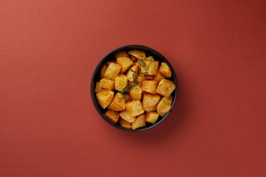 Siyah bir tabakta kırmızı bir arka planda üst çekim, doğranmış patates, rustik stil, biberiye serpiştirilmiş, aromatik yan yemek Avrupa mutfağı