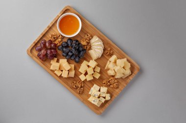 Tahta bir tahtanın üzerindeki gri bir arka planda kırmızı üzüm, bal ve şarapla birlikte ceviz iştah açıcı sunan büyük bir şirket için çeşitli peynirler sunuluyordu.