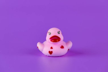 Bu sevimli pembe plastik ördek neşeli kalp tasarımları içeriyor, cesur mor bir zemin üzerine kurulmuş, çocukluk keyfi ve eğlencesi için bir eğlence ve nostalji hissi uyandırıyor..