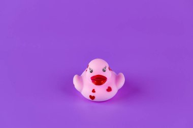 This delightful pink rubber duck features charming red heart accents on its body, set against a vivid purple background, perfect for children's playtime or as a cute decorative item. clipart