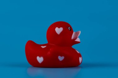 Bu hoş görüntü, neşeli kalp desenleriyle süslenmiş kırmızı kauçuk bir ördeği canlandırıyor, canlı mavi bir zemin üzerine kurulmuş, neşeli bir dekor içinde neşe ve nostalji uyandıran.