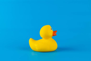 Parlak sarı renkli sevimli ve renkli bir ördek, parlak mavi bir arka plana karşı mükemmel bir şekilde konumlandırılmış, çocuklar için neşeli ve neşeli banyo zamanı anılarını canlandırıyor..