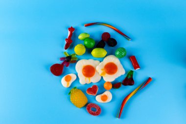 Bu resim, mavi bir yüzeyde, yiyeceklerden ve meyvelerden esinlenerek sanatsal şekilleri vurgulayan, canlı şekerler ve şekerler sergiliyor..