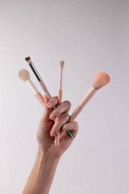 Görüntü, dört farklı makyaj fırçasını tutan bir insanın elini gösteriyor. Çekici tasarımlarını ve makyaj rutinlerinde harmanlamak, uygulamak ve çevrelemek için uygun yumuşak tüylerini vurguluyor..