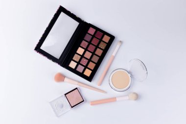 Bu resim, çeşitli tonları olan zarif bir makyaj paleti sergiliyor. Yanında fırçalar ve pudra pudrası da var. Güzellik meraklıları ve profesyoneller için ideal..