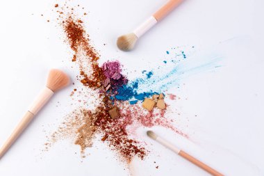 Makyaj tozları ve fırçalardan oluşan sanatsal bir düzenleme temiz beyaz bir arkaplana saçılmış ve güzellik ürünleri için ideal renk ve dokuların rengarenk bir karışımını sergiliyor.