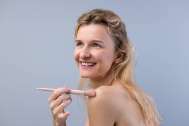 Gülümseyen bir kadın, omuzunda narin bir fırçayla makyaj yapmaktan zevk alır. Özgüvenini ve güzelliğini kutlar. Basit, havadar bir arka planda geçer..