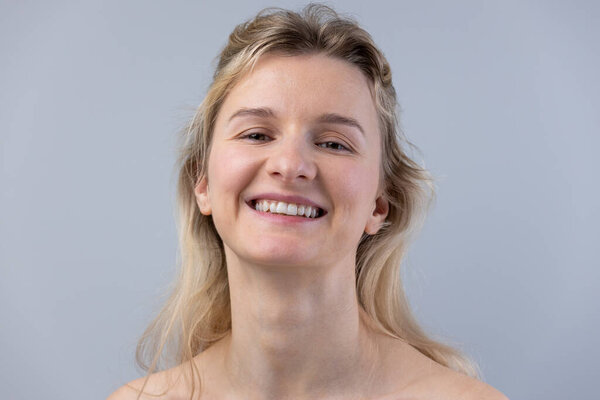 The image features a smiling young woman with light blonde hair, radiating joy and confidence. The neutral gray background highlights her vibrant expression and natural beauty.
