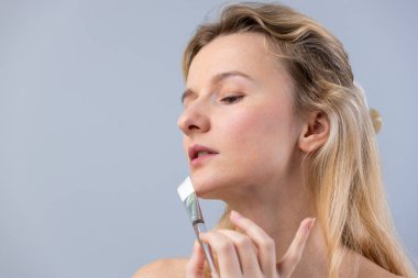 Görüntü, doğal güzelliğin gelişimi için cilt bakımının ve cilt bakımının önemini vurgulayan bir kadının nazikçe yüzüne sürdüğü bir cilt bakım ürünü içeriyor..