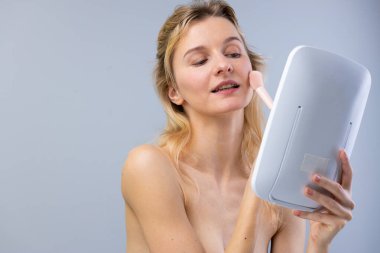 Görüntü, zarif bir dokunuşla kızaran genç bir kadını, güzel ve taze bir görünüme olan bağlılığını sergileyerek, parlak bir aynada çalışmalarına hayran bırakıyor..