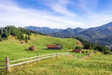 Berrak mavi bir gökyüzü altında yemyeşil ve görkemli dağlarla çevrili geleneksel ahırlar ve samanlıklarla benekli güzel tepeler..