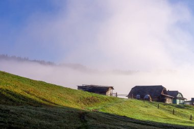 Zarif sabah sisinden doğan büyüleyici kır evleri sergilenen pitoresk bir manzara. Bereketli yeşil tepeler, kırsal hayatın güzelliğini yansıtan huzurlu bir zemin oluşturur..