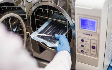 Laboratuvar önlüklü bir kişi, B sınıfı sterilizatöre giden sterilize tıbbi gereçlerle dolu bir paketle ilgileniyor. Sağlık hizmetlerindeki önemli hijyen uygulamalarını gösteriyor..